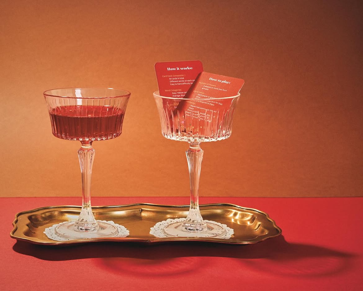 Two crystal coupe glasses on a gold tray, one holding red 'How it works' and 'How to play' Munka rule cards
