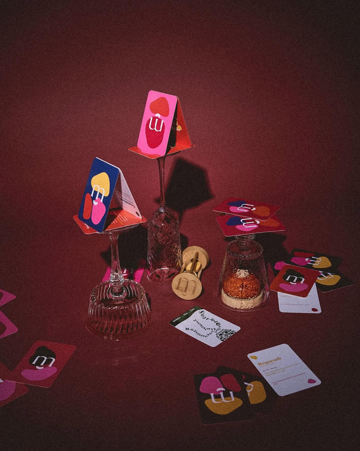 Munka cards balanced on stacked wine glasses against a deep red background