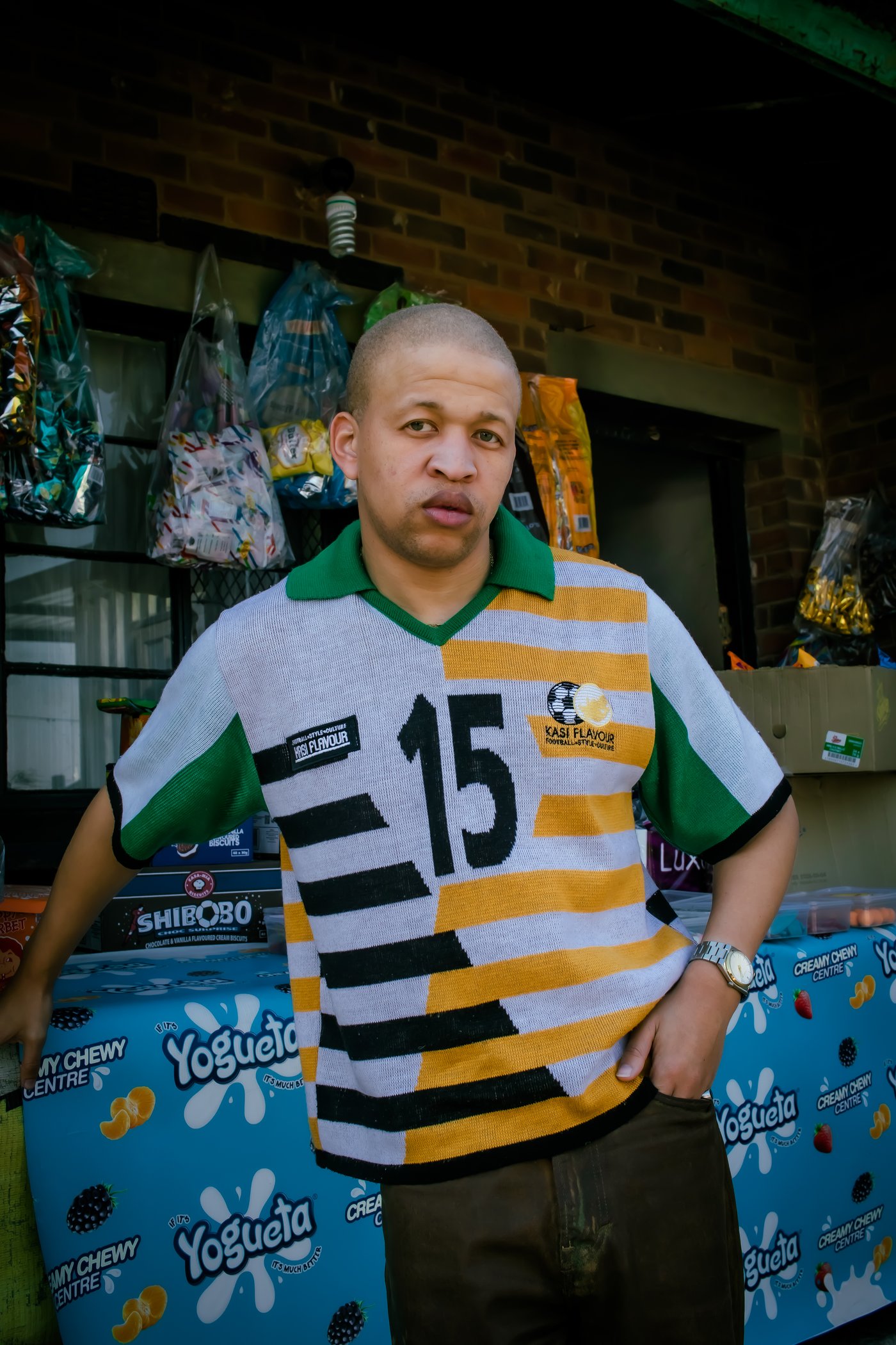 From Daily Click: man in white, yellow and green number 15 Kasi Flavour jersey outside a spaza shop
